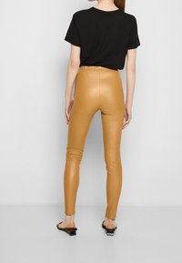 Leggings en simili cuir beige à taille haute, coupe slim et texture lisse, associés à un t-shirt noir à manches courtes et des sandales simples.