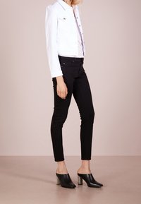 Bílá zkrácená džísková bunda, černé skinny džíny a černé muly s kovovými čtvercovými podpatky. Jasný tvar a dobře padnoucí střih po celé délce.