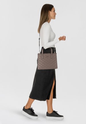 Sac à main matelassé gris avec deux poignées supérieures et une bandoulière amovible. Le modèle porte un haut blanc et une jupe noire, associés à des baskets.