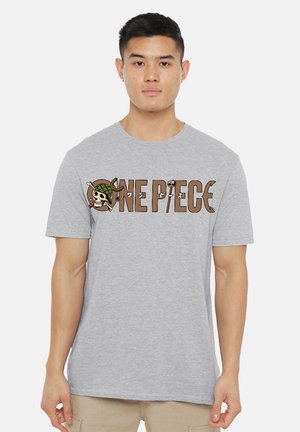 Young man wearing a light grey t-shirt with a brown "ONE PIECE" logo featuring a skull with a green helmet.