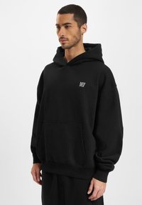 Czarna, oversize bluza z kapturem, wykonana z mieszanki bawełny, z przednią kieszenią, ściągaczami u rękawów oraz białym logotypem "DEF" na lewej piersi.