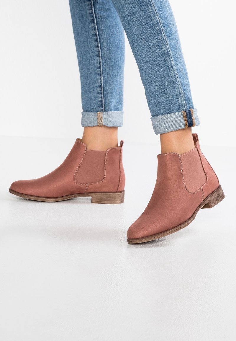 Rosa Knöchelstiefel aus glattem Stoff, mit elastischen Seiteneinsätzen und einem niedrigen Holzabsatz. Getragen mit hochgekrempelten blauen Jeans.