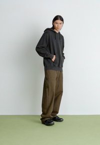 Dark gray hoodie with a kangaroo pocket, paired with loose-fitting, olive green cargo pants. Black sneakers complete the outfit.