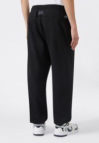 Czarne dresy z wiązaniem w pasie, prostym krojem nogawek i kieszeniami po bokach. Noszone z białymi trampkami z czarnymi akcentami.