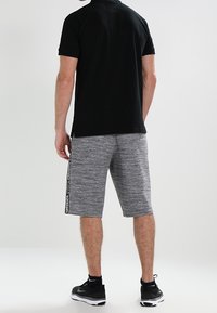 Mörkblå kortärmad polo t-shirt för män, som matchas med grå, knälånga shorts med en strukturerad design och sidobranding. Svarta sportskor.