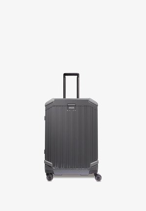 Maleta rígida de color gris oscuro con ranuras verticales, asa retráctil y cuatro ruedas giratorias para facilitar la maniobrabilidad.