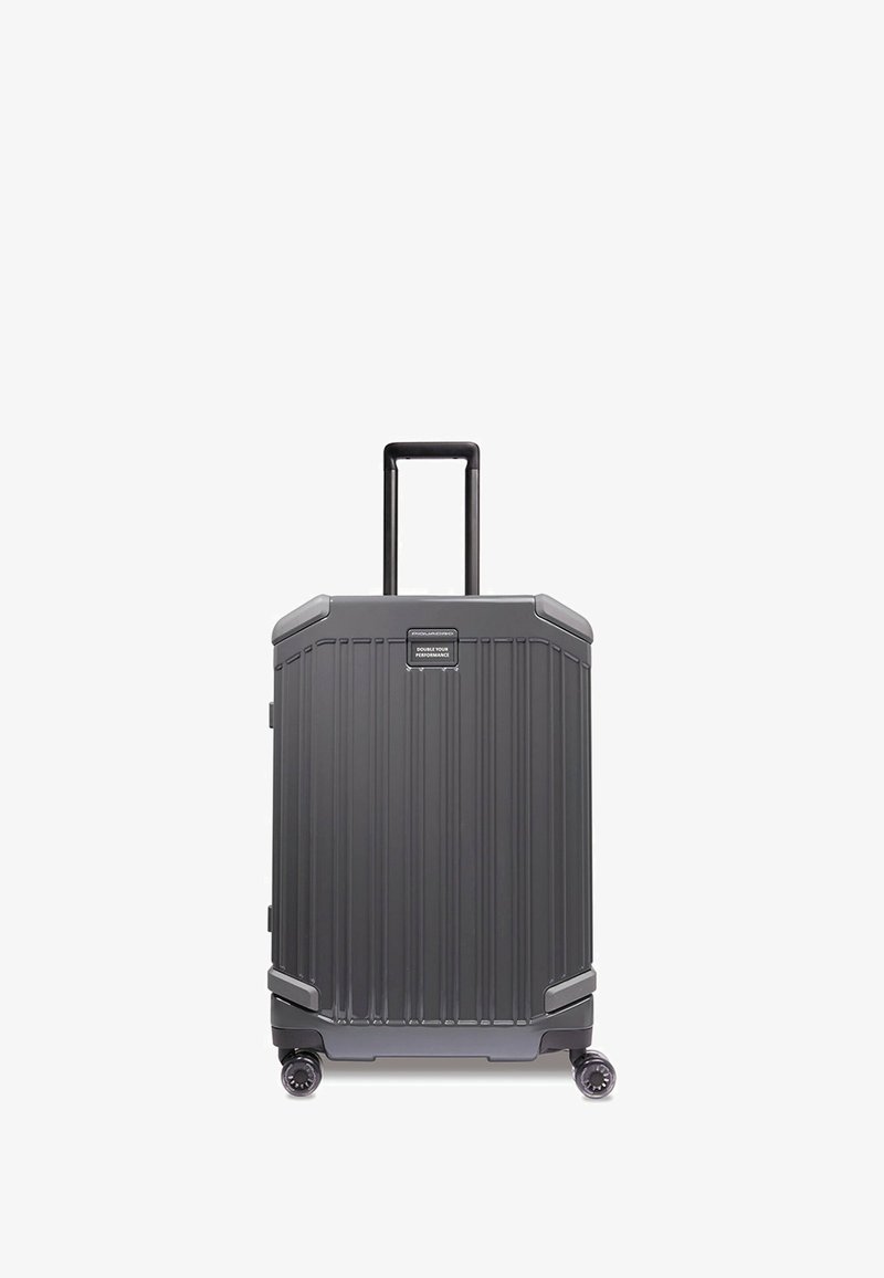 Valigia rigida di colore grigio scuro con scanalature verticali, manico retraibile e quattro ruote girevoli per una facile manovrabilità.