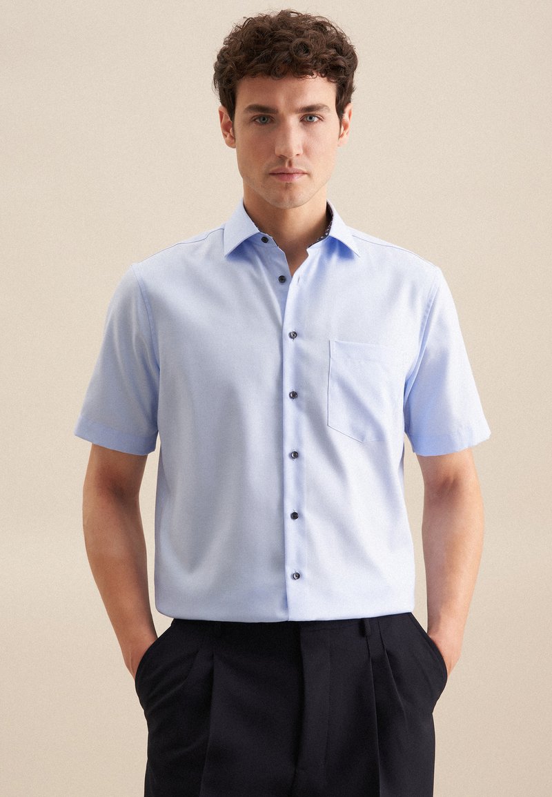 Camicia a maniche corte azzurro chiaro con colletto button-down, bottoni neri e taschino sul petto. Tessuto morbido e vestibilità aderente.