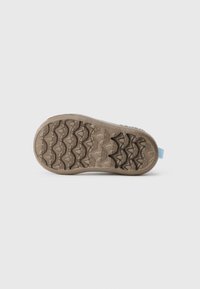 Semelle de chaussure brune avec une surface en caoutchouc texturé présentant un motif en zigzag. Accent bleu clair sur le talon. Forme plate et ronde.