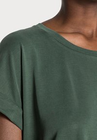 Grön, kortärmad topp med vid halsringning. Tillverkad av mjukt tyg, har den en avslappnad passform och slät yta.