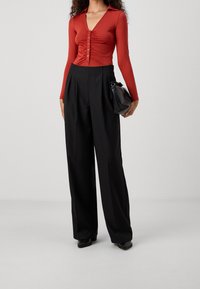 Czerwony dopasowany top z długim rękawem, dekoltem w serek i detalami z guzikami, zestawiony z czarnymi spodniami o szerokich nogawkach z wysokim stanem oraz małą czarną torebką.
