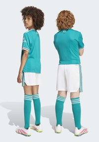 Türkis jalad ja valged lühikesed püksid, triibulised teal-sokid, küljel kolm triipu ja roosa aktsendiga spordijalatsid.