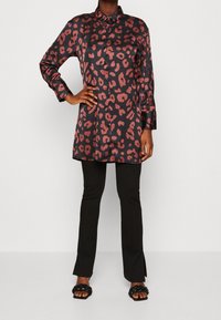 Robe chemise en satin avec un imprimé léopard noir et bordeaux, manches longues, boutonnière à l'avant et coupe droite, associée à un pantalon noir ajusté.