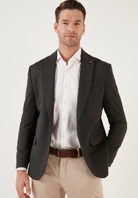 Blazer grigio scuro con un motivo a trama, bottone singolo, rever a scatto e due tasche laterali, abbinato a una camicia bianca e pantaloni beige.
