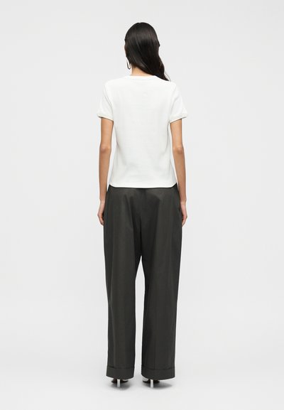 Λευκό μπλουζάκι με ριγμένα μανίκια, σε συνδυασμό με άνετο, σκουρό γκρι παντελόνι με γυρισμένο τελείωμα, υπογραμμίζοντας τον απλό και λειτουργικό σχεδιασμό.