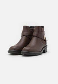 Bottes courtes en cuir marron avec un petit talon carré, dotées d'une fermeture éclair latérale, d'une sangle décorative et d'un accent en métal doré.