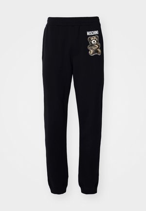Čierne tepláky vyrobené z bavlny s elastickým pásom, s grafikou medvedíka a textom "MOSCHINO" po stranách.