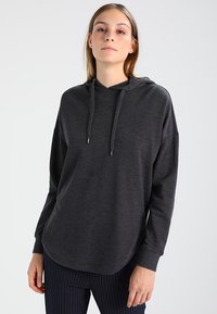 Sweatshirt à capuche gris foncé avec une coupe décontractée, des manches longues, un cordon de serrage pour la capuche et une texture douce, associé à un pantalon à rayures.