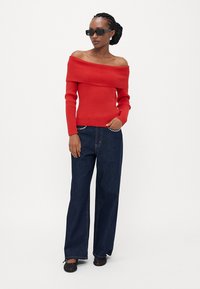 Rød ripet off-shoulder genser kombinert med mørkeblå vide jeans. Ensemblet har chunky svarte solbriller og flate sko.
