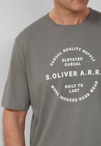 Grijze katoenen t-shirt met ronde halslijn en korte mouwen. Bevat witte tekst in een cirkelvormige lay-out die het merk en slogans verklaart.