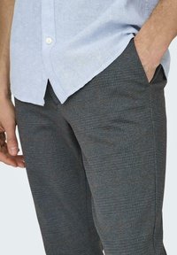 Grå teksturerede bukser med et subtilt ternet mønster, der har sidelommer og en slim fit, parret med en lyseblå, kortærmet skjorte.