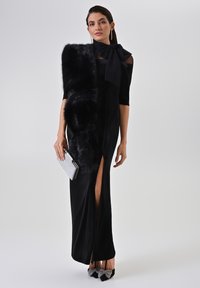 Zwarte avondjurk met een nauwsluitend silhouet, voorzien van een hoge split tot op de dij, gecombineerd met een nepbont stola en een zilveren clutch. Hakken met strikdetail.