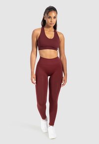 Bordowy sportowy biustonosz z prążkowaną teksturą oraz legginsy z wysokim stanem w dopasowanym kolorze. Białe trampki podkreślają sportowy strój.