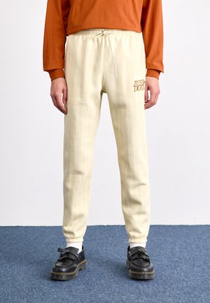 Beige pinstriped sweatpants with an elastic waistband and drawstring; features an embroidered "JUST DON'T" logo in orange.