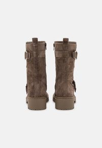 Botas de tobillo de ante marrón con un acabado texturizado, cierre de cremallera en la parte posterior y acentos de hebilla en los laterales. Suela de goma plana con un patrón de relieve definido.