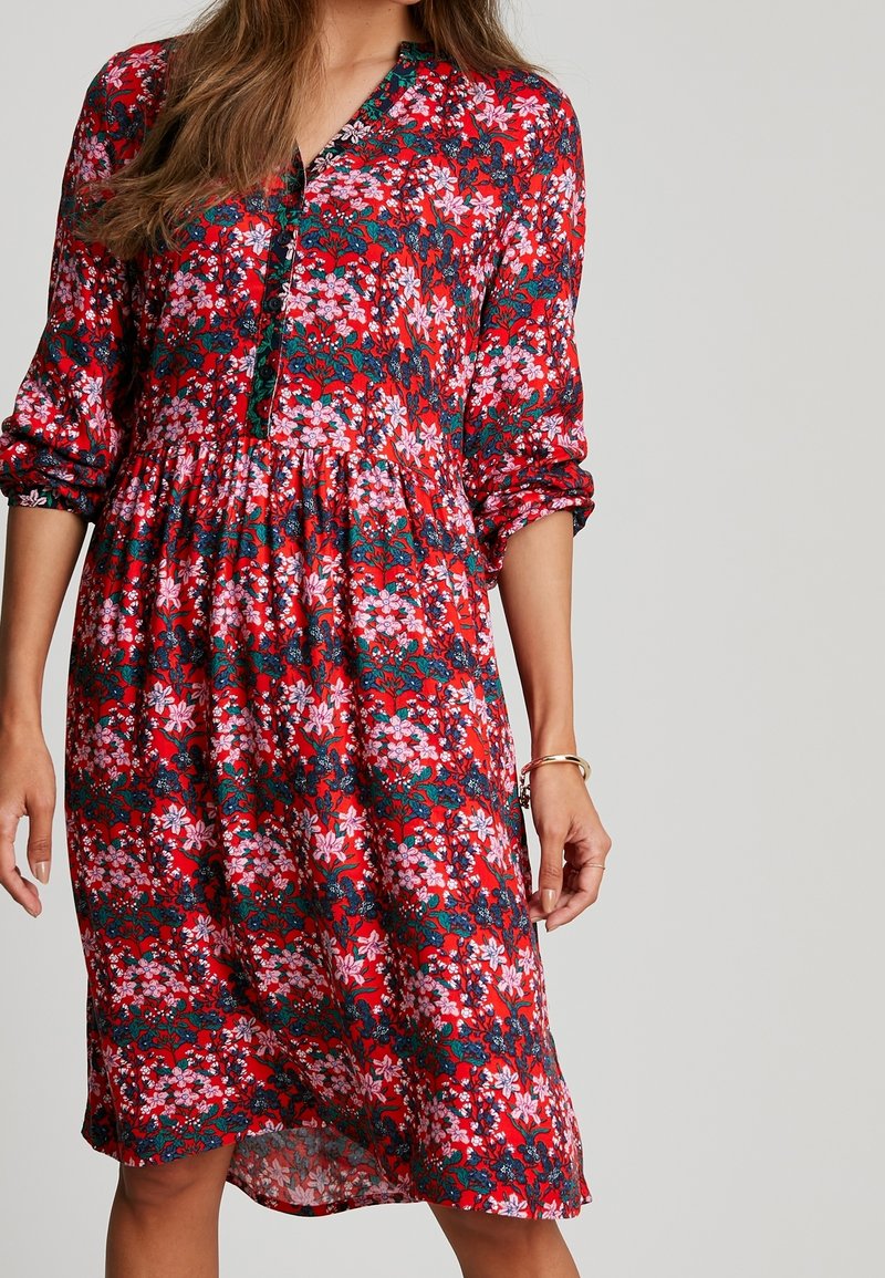Czerwona kwiatowa sukienka z rękawami do trzech czwartych, z guzikowym dekoltem, zebraną talią i żywym połączeniem różowych i zielonych wzorów.