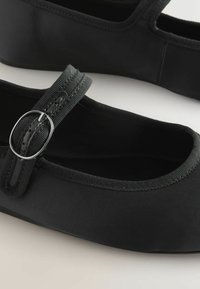 Ballerines noires en tissu doux, avec un bout rond, une sangle ajustable avec une boucle en métal argenté et une texture lisse.