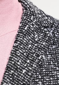 Black and white tweed fabric with a textured, woven pattern, layered over a light pink turtleneck sweater.