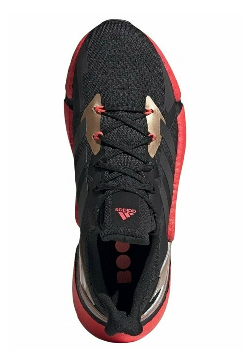 Chaussure de sport noire avec des accents rouges, tige en tissu tricoté, détails dorés proéminents sur les côtés et semelle texturée. Logo sur la languette.
