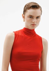Top sin mangas rojo con un escote alto, hecho de una tela suave y elástica, que presenta un diseño ajustado y costuras mínimas para un aspecto elegante.