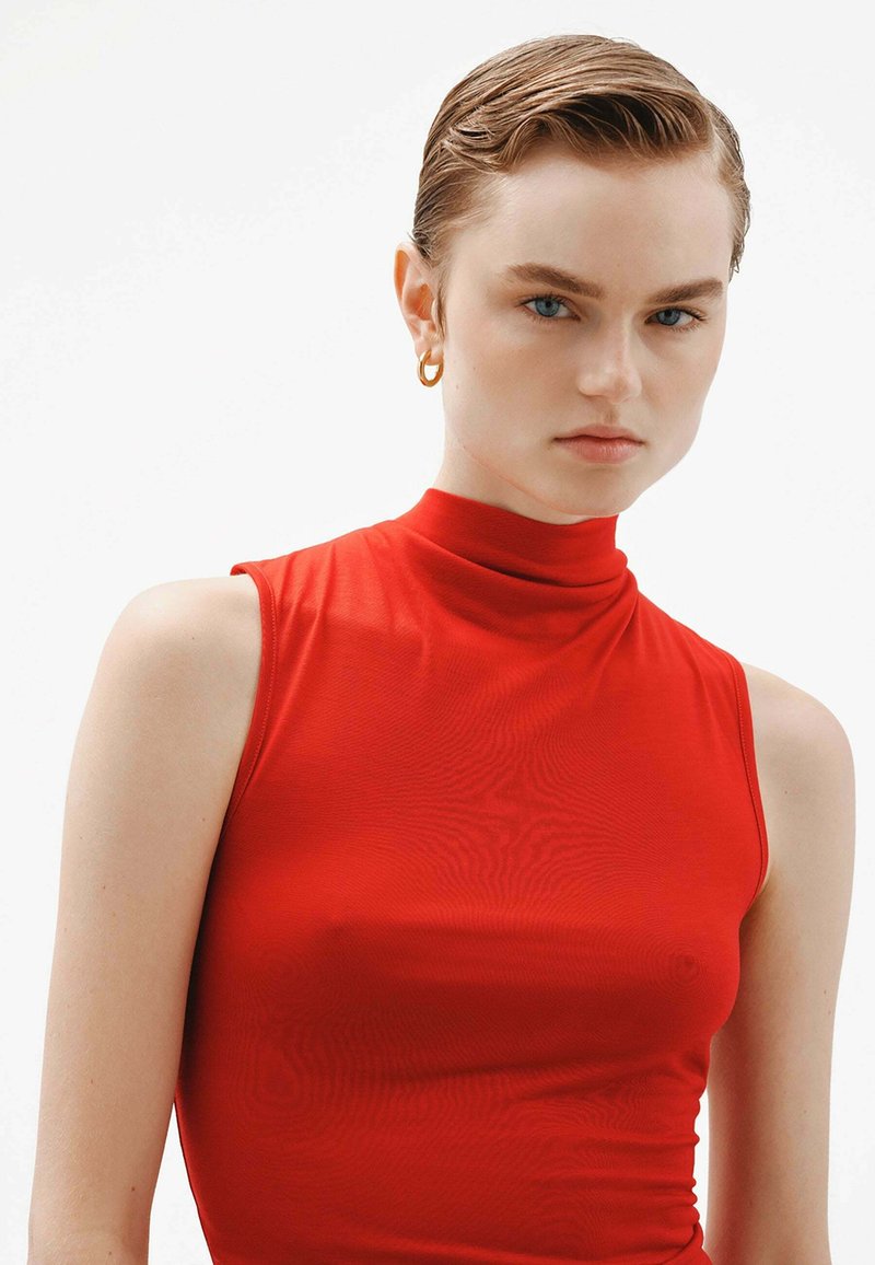 Top sin mangas rojo con un escote alto, hecho de una tela suave y elástica, que presenta un diseño ajustado y costuras mínimas para un aspecto elegante.