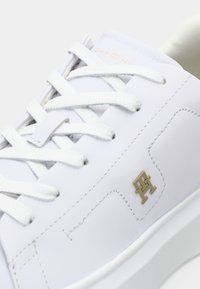 Sneaker in pelle bianca con lacci bianchi, logo dorato "TH" sul lato e discreta marcatura "Tommy Hilfiger" sulla linguetta.