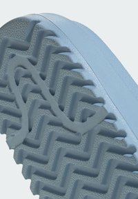 Gros plan sur une semelle de chaussure en caoutchouc grise avec un motif de bande de roulement en zigzag et une surface texturée pour l'adhérence.