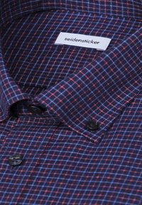 Chemise à col avec un motif à carreaux bleu, rouge et noir, montrant une étiquette blanche portant la mention "seidensticker" à l'intérieur du col.