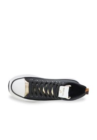 Zapatilla de lona negra con puntera blanca brillante, acentos metálicos, cordones negros y lengüeta blanca con marca. Diseño de suela plana.