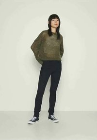 Olivnozeleni pleteni pulover z ohlapnim fitom in odprtim vzorcem, parjen z črnimi skinny jeans in črnimi teniskami Converse.