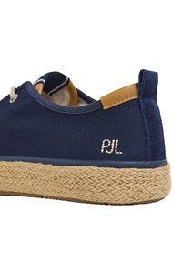 Scarpa di tela blu navy con accentuazione in pelle beige, suola in corda intrecciata naturale e dettaglio ricamato "PJL" sul retro. Design arrotondato con lacci frontali.