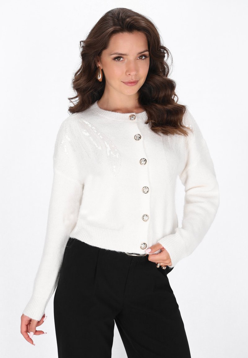Cardigan alb tricotat, cu guler rotund, închis cu nasturi, ornamentat cu paiete pe umeri, având mâneci lungi și mansete cu model în dungi.