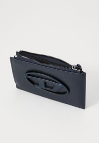 Navy leather wallet with a zip closure, featuring a raised oval logo and contrasting stitching. Smooth texture with dark zipper.