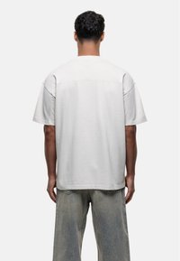 Unisex oversized T-shirt met korte mouwen in lichtgrijze katoen. Voorzien van een ronde hals en minimale stiksels. Draagt bij lichte denim.