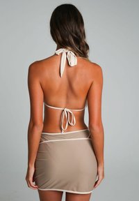 Beige bikini top met halterstrikken, gecombineerd met een bijpassende rok met een semi-doorzichtige uitstraling en contrasterende rand. Glad textuur.