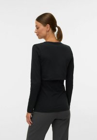 Crna dugorukava majica s krojenjem koje je skraćeno straga, s okruglim izrezom i glatkom teksturom.