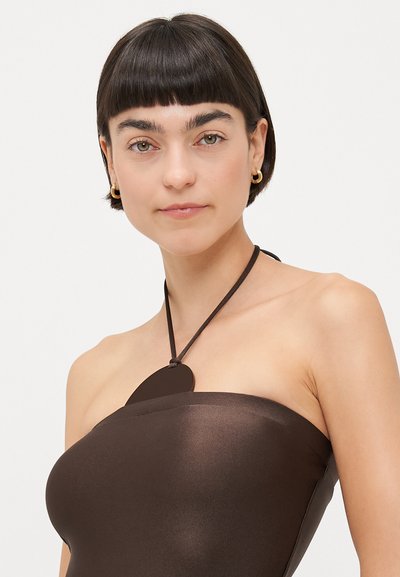 Brown strapless top, smooth sheen fabric, featuring a round accent secured with a thin strap. Minimalist design emphasizes simplicity and elegance.