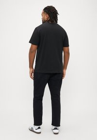 Μαύρο κοντομάνικο μπλουζάκι, απλό σχέδιο, με στρογγυλή λαιμόκοψη. Συνδυασμένο με μαύρο παντελόνι και λευκά αθλητικά παπούτσια με μαύρες ρίγες.