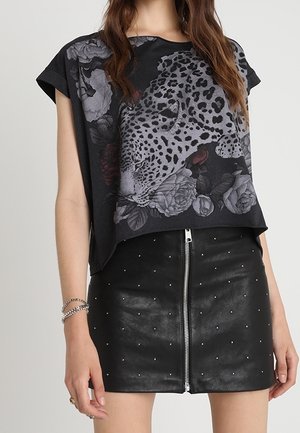 Kobieta w czarnej krótkiej koszulce z nadrukiem w panterkę i kwiaty, w połączeniu z czarną mini skórzaną spódnicą z przednim suwakiem i ćwiekami.