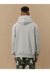Gray hoodie with a large, soft hood. Made of textured fabric, featuring a relaxed fit and ribbed cuffs. Paired with patterned green pants.
